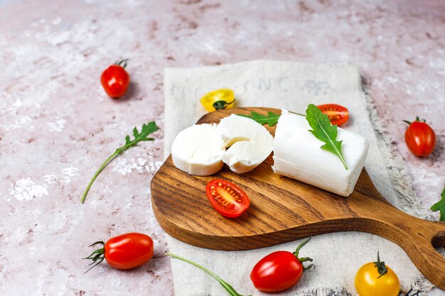 Fatias de queijo de cabra na placa de madeira com ruccola, tomate cereja. Pronto para comer.