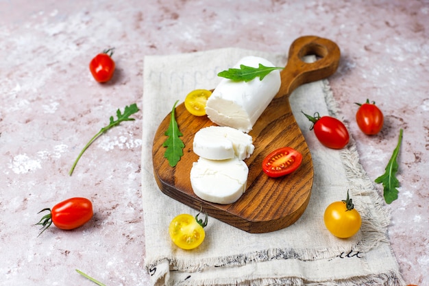 Fatias de queijo de cabra na placa de madeira com ruccola, tomate cereja. Pronto para comer.