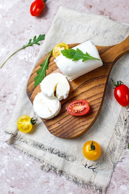 Fatias de queijo de cabra na placa de madeira com ruccola, tomate cereja. Pronto para comer.