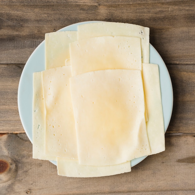 Fatias de queijo no prato branco contra o pano de fundo de prancha de madeira