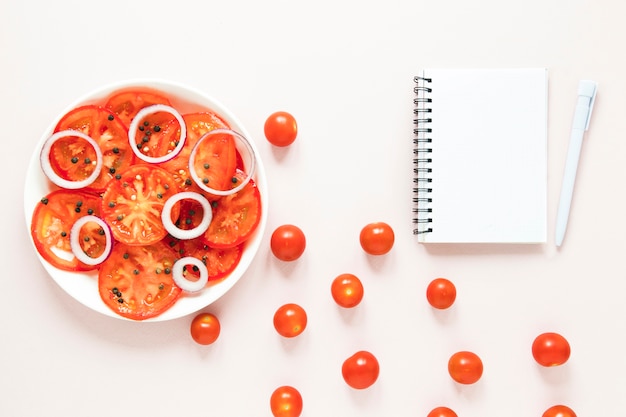 Foto grátis fatias de tomate e cebola ao lado do caderno vazio