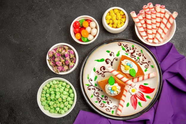 Fatias de torta cremosa de vista de cima com tecido roxo e doces em um espaço cinza