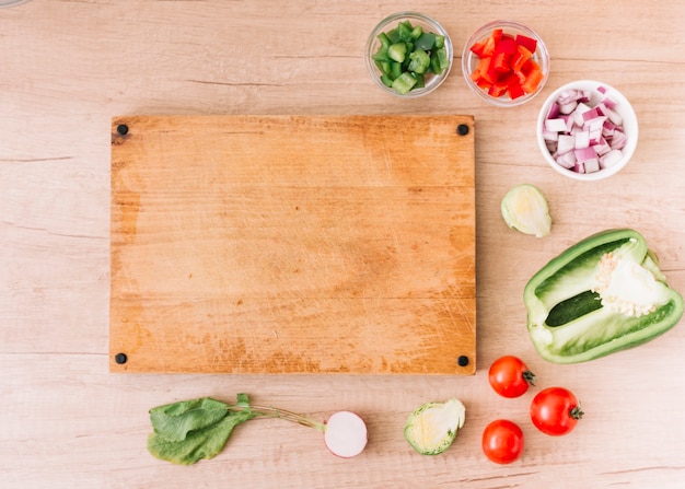 Fatias de vermelho; pimentão verde; cebola; beterraba; tomates cereja perto da tábua em branco sobre a mesa de madeira