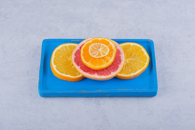 Fatias redondas de toranja fresca, laranja e limão na placa azul.