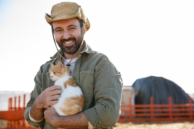 Fazendeiro segurando um gato adorável enquanto visita sua fazenda