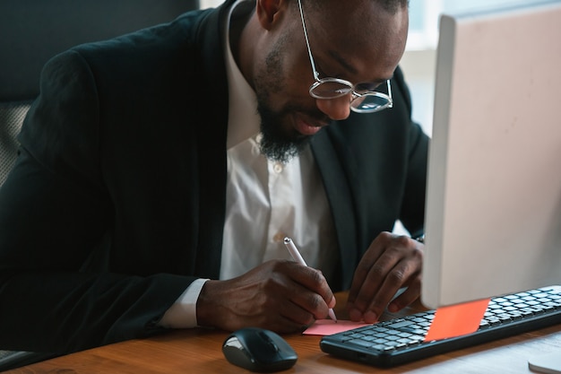 Foto grátis fazendo anotações. empreendedor afro-americano, empresário trabalhando concentrado no escritório. parece serio e ocupado, vestindo terno clássico, jaqueta.