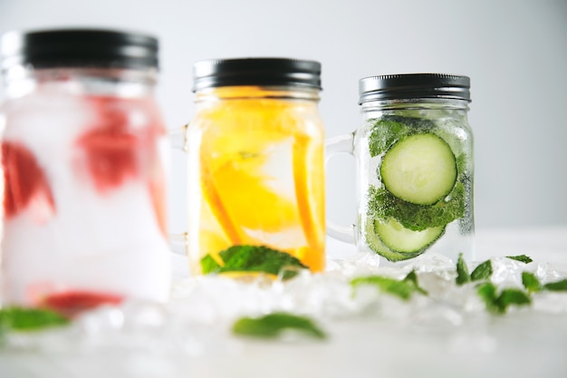 Foto grátis fechar o foco na última jarra limonadas caseiras frescas e saudáveis com água com gás morango, pepino, hortelã e laranja isoladas em cubos de gelo esmagados na mesa de madeira