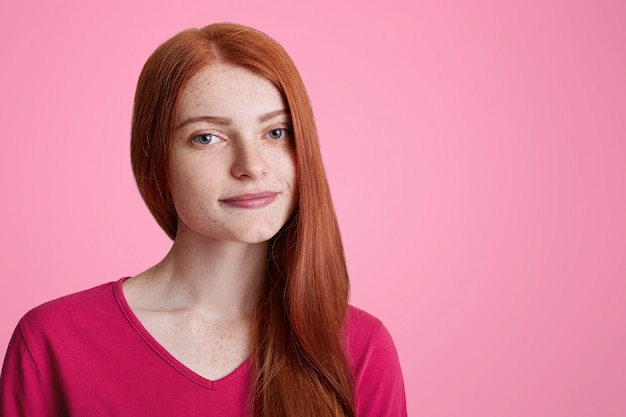 Fechar o retrato da fêmea jovem sardenta veste casual camisola rosa, olha com confiança para a câmera, sonha com algo