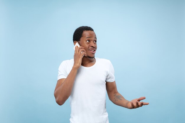 fechar o retrato de um jovem afro-americano de camisa branca ... Falando ao telefone, segurando um smartphone.