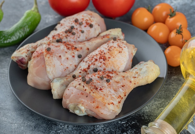 Feche a foto coxa de frango cru na placa preta com legumes frescos.