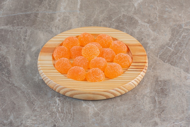 Feche a foto de doces de geleia de laranja sobre a placa de madeira.