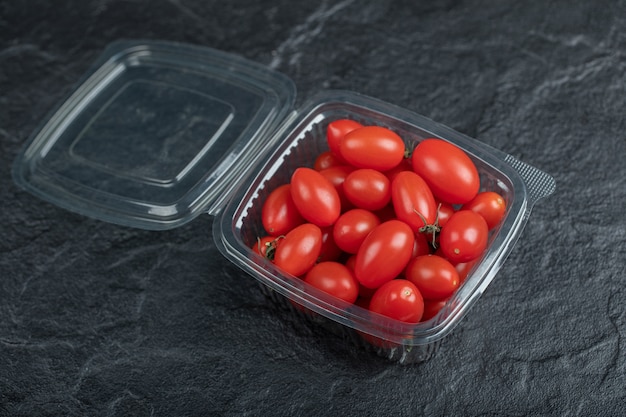 Feche a foto de pequenos tomates vermelhos em um recipiente de plástico em um recipiente preto. Foto de alta qualidade