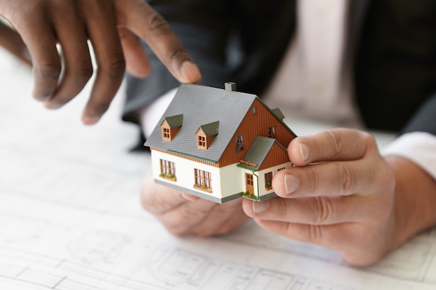 Foto grátis feche a foto de um empreiteiro caucasiano segurando um projeto imobiliário enquanto seu colega africano apontando o dedo para o edifício da maquete, explicando o projeto durante a reunião de apresentação no escritório