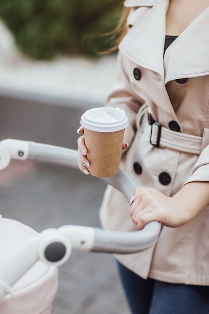 Feche a foto, mulher segurando a xícara de café descartável e ficar no carrinho de bebê.
