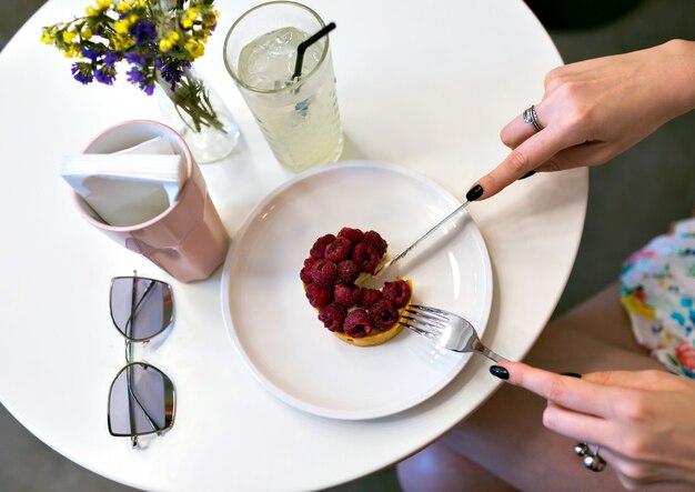 Feche a imagem das mãos da mulher que cortam o saboroso bolo de framboesa, imagem de café, manicure elegante, cores suaves em tons, desfrute da sobremesa, conceito de nutrição de dieta.