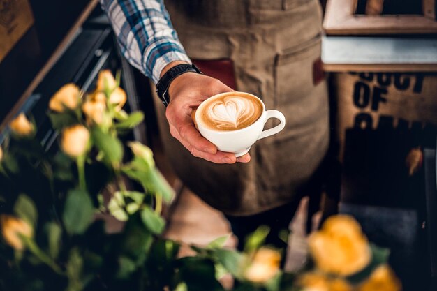 Feche a imagem de um homem segurando um café com uma vista superior de espuma de coração.