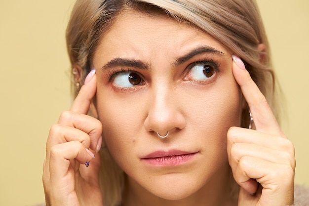 Feche a imagem de uma jovem mulher caucasiana frustrada com a testa franzida, segurando os dedos nas têmporas, pensando muito em algo, tendo dor de cabeça ou enxaqueca. Garota fofa descontente dizendo: Use seu cérebro