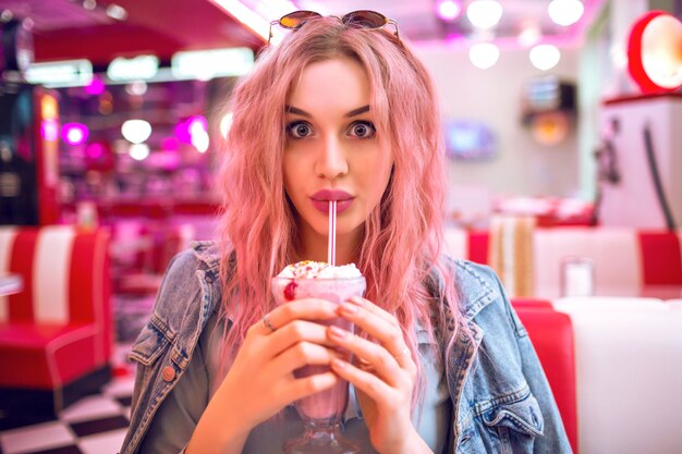 Feche a imagem de uma mulher segurando um milk-shake de morango doce, pin up estilo retro, cores pastel, café americano vintage.