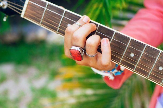 Feche a imagem de uma mulher tocando violão, accessorizes brilhantes, fundo de palmas verdes.