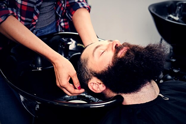 Feche a imagem do cabeleireiro feminino lavando o cabelo dos homens barbudos antes do corte de cabelo em um salão.