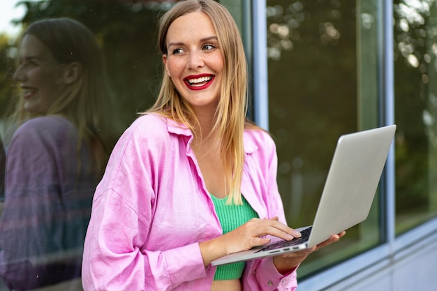Feche a imagem horizontal de uma mulher loira elegante usando seu laptop, brilhante compõem o humor positivo, trabalho e estudo.