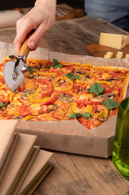 Feche a mão cortando pizza com ferramenta