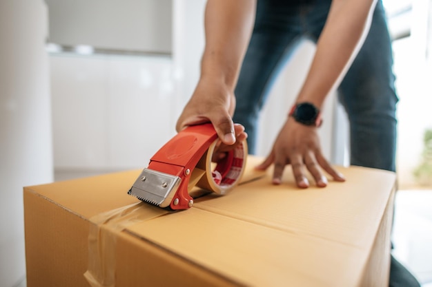 Feche a mão do homem use fita adesiva para fechar a caixa de papelão selando a caixa grande para embalar o conceito de nova casa em movimento Foco seletivox9caixa de papelão