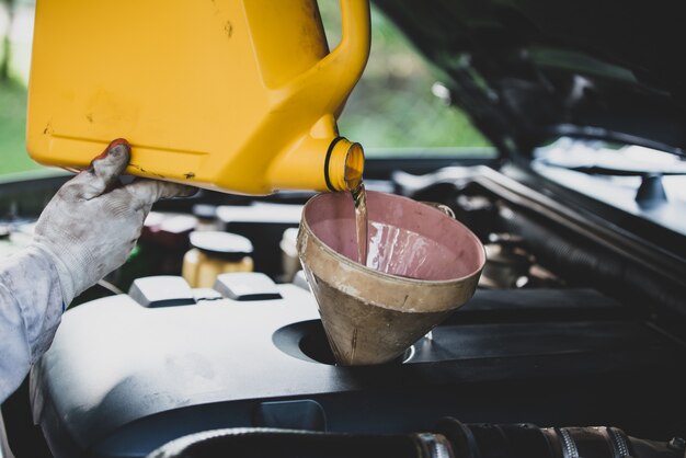 Feche a mão do mecânico de automóveis, derramando e substituindo o óleo fresco no motor do carro na garagem de reparação de automóveis. Manutenção de automóveis e conceito da indústria