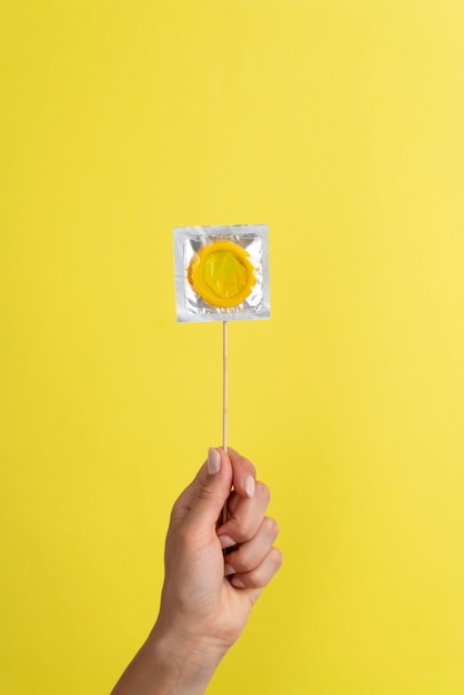 Feche a mão segurando um preservativo amarelo