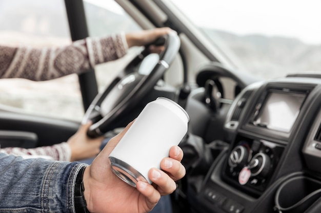 Feche a mão segurando uma lata de refrigerante no carro