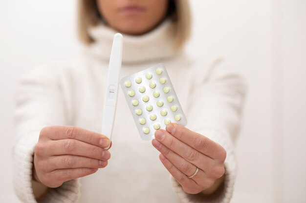 Feche a mulher segurando pílulas e teste de gravidez
