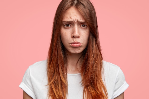 Feche acima da foto de mulher carrancuda e bonita faz beicinho, tem uma expressão triste, isolada no fundo rosa.