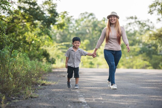 Feche acima da mamã feliz e do filho que guardam a mão em um parque. Conceito de família.