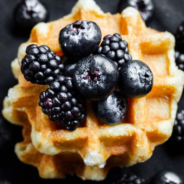 Feche acima das frutas da floresta negra em waffles