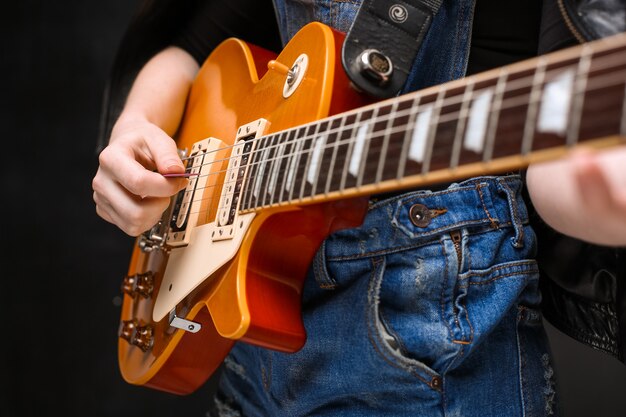 Feche acima das mãos da menina na guitarra sobre fundo preto.