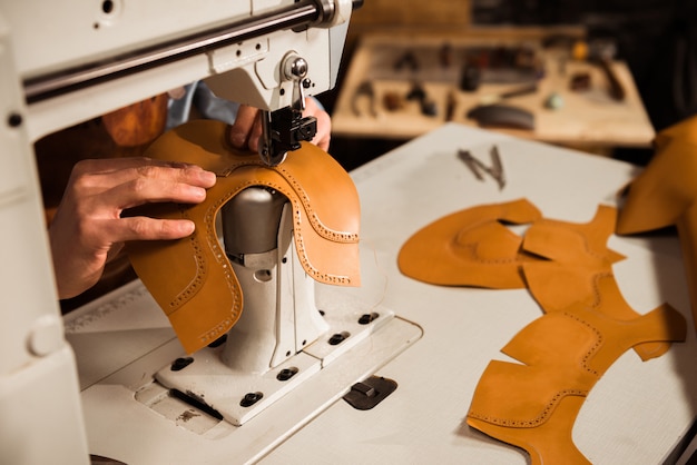 Foto grátis feche acima de um artesão masculino que costura as peças de couro