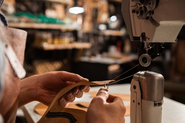 Feche acima de um sapateiro usando a máquina de costura