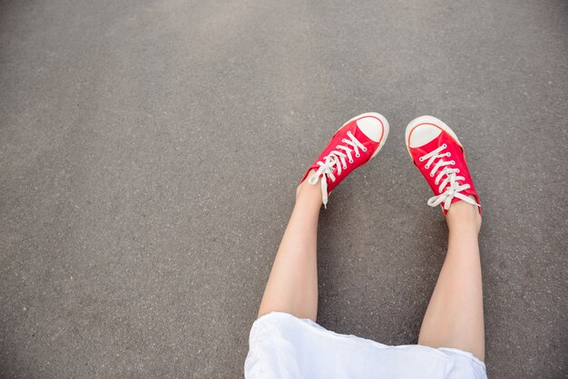 Feche acima dos pés nos keds vermelhos que encontram-se no asfalto.
