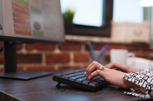 Feche as mãos do funcionário da agência de publicidade digitando no teclado e trabalhando em gráficos de pesquisa. Trabalhador de escritório da empresa usando computador para desenvolver estratégia de marketing e carteira de clientes de negócios.