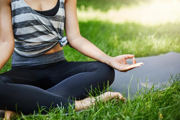 Feche as mãos femininas sentadas em lotus asana perseguindo zen em um dia ensolarado de verão