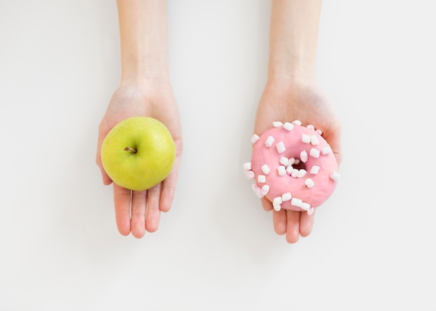 Foto grátis feche as mãos segurando um donut e uma maçã
