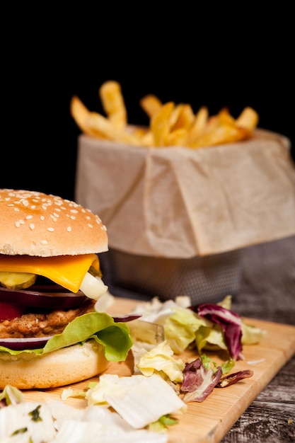 Feche de delicioso hambúrguer caseiro na placa de madeira ao lado de batatas fritas. Comida rápida. Lanche não saudável