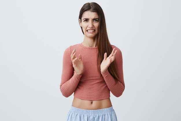 Feche de encantadora jovem caucasiana bonita com cabelos castanhos compridos em roupa elegante, espalhando as mãos com expressão de nojo, depois de ver o dente na comida durante a refeição no restaurante.