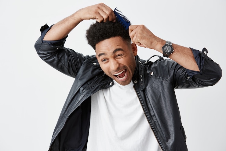 Foto grátis feche de infeliz jovem de pele escura com penteado afro em camiseta branca sob a jaqueta de couro, gritando de dor quando pente emaranhado em seus cabelos, chegar atrasado para o trabalho.