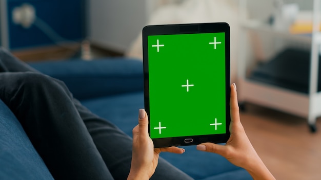 Feche de mãos de mulher de negócios segurando um computador tablet com simulação de visor chave de croma de tela verde, sentado no sofá. Freelancer usando dispositivo touchscreen isolado para navegação em redes sociais