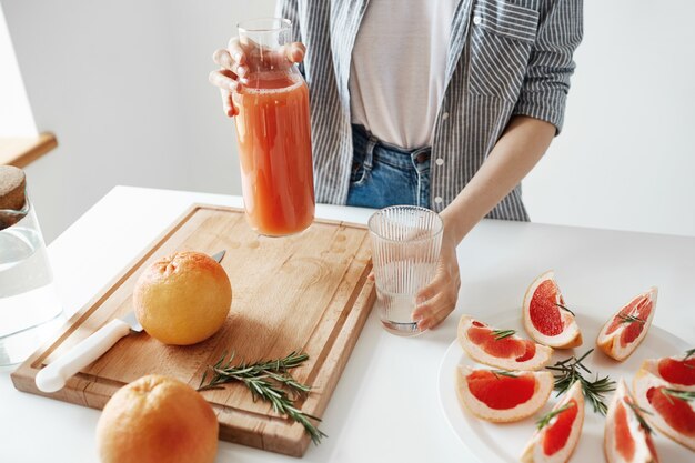 Feche de menina segurando o frasco de vidro com suco de desintoxicação de toranja no café da manhã. Conceito de nutrição saudável.