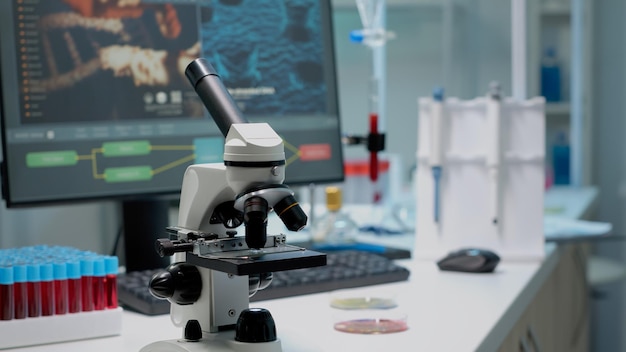 Feche de microscópio químico e equipamentos de pesquisa médica em laboratório científico. Ferramenta de exame de líquido com lente de vidro e amostras de sangue em vacutainers em mesa profissional