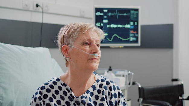 Feche de mulher aposentada com tubo de oxigênio nasal à espera de assistência. Retrato de pessoa com doença respiratória com monitor de frequência cardíaca para medição de pulso na enfermaria do hospital