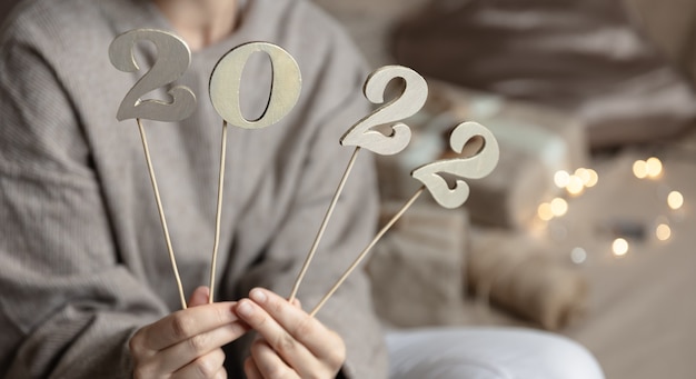 Foto grátis feche de números de madeira 2022 em varas em mãos femininas no fundo desfocado com bokeh.