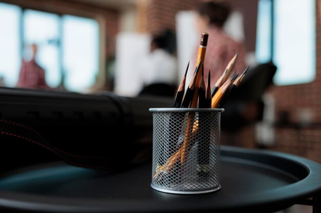 Feche de pé de lápis gráfico em pé na mesa no estúdio da escola de criatividade. Em segundo plano, equipe diversa desenhando esboço de vaso em tela trabalhando na técnica de desenho. Resoluções de ano novo